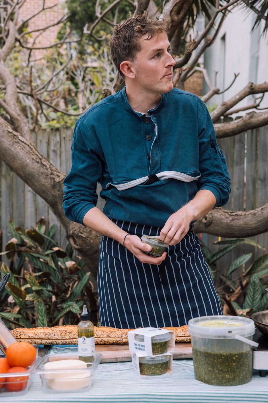 Ed, Crush's founder, in his apron with a pot of pesto, looking off to the side behind a table of Crush pots and a 2kg tub