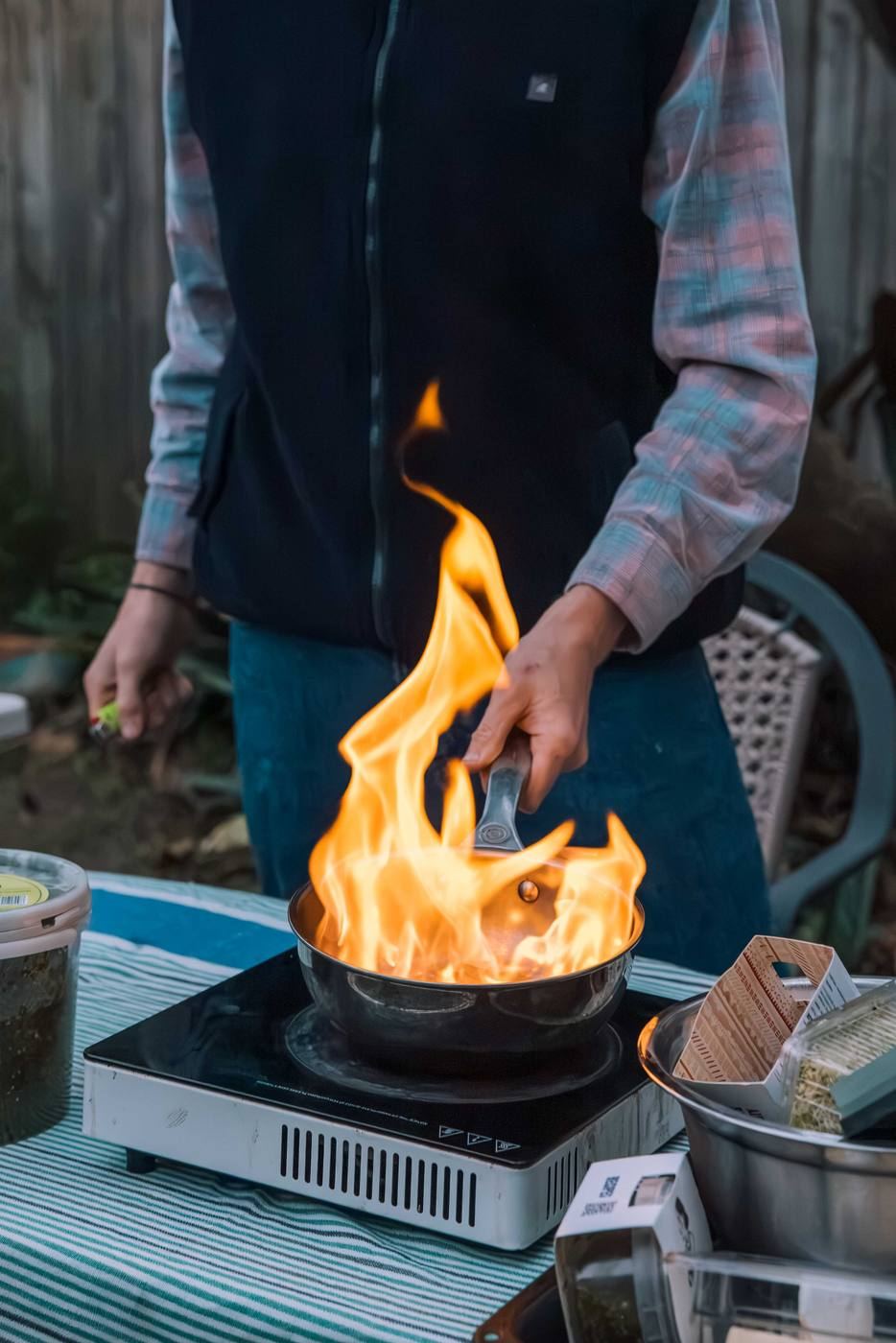 A chef flaming a pan on an outdoor burner