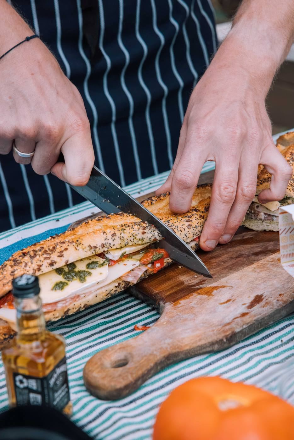 A chef slicing a seeded baguette filled with pesto